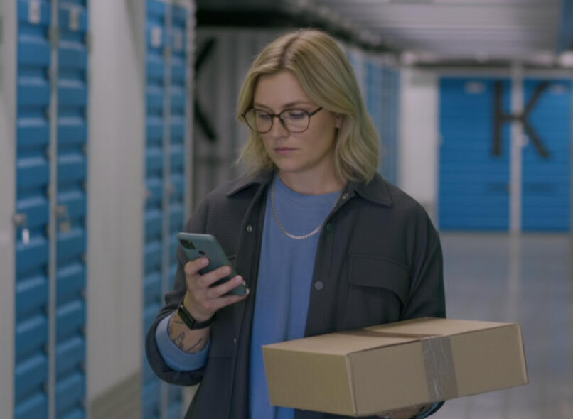 Customer carrying a storage box while walking down an aisle of clean indoor storage units at Locked Self Storage Alloa.
